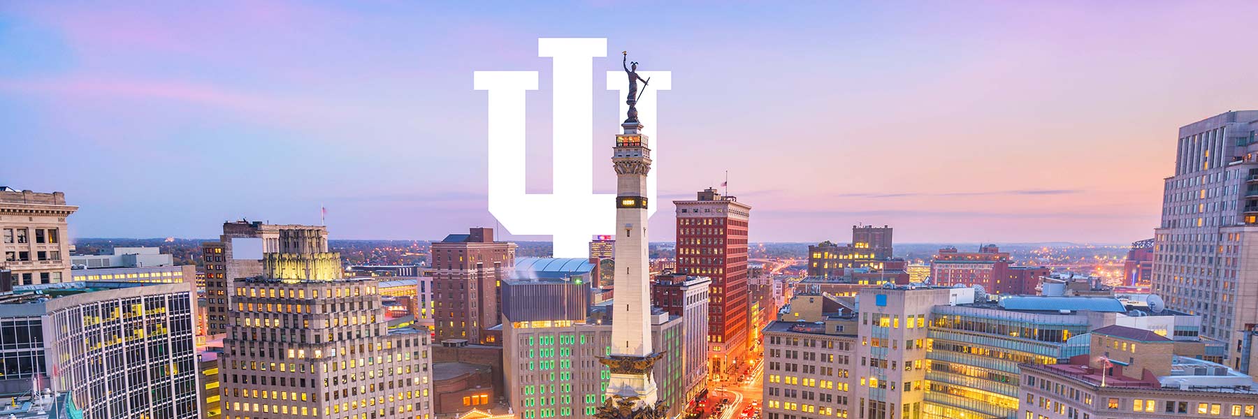 The Indianapolis skyline and Circle Center Monument are pictured during a colorful sunset, IU's trident logo is placed within the skyline.