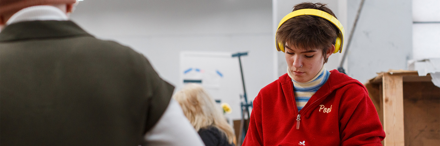 A student wearing a crimson jacket and large yellow earphones works on a project in the Herron School of Art + Design