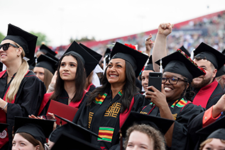 A crowd of female and male students participate in the undergraduate commencement ceremony at Carroll Stadium. One students is recording the event with her phone.