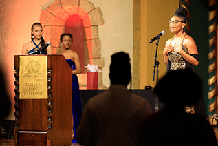 A student sings "Lift Every Voice and Sign", also known as the Black National Anthem, during the Martin Luther King Junior Celebration Dinner at the Indiana Roof Ballroom. Two student MCs are in the background behind a podium