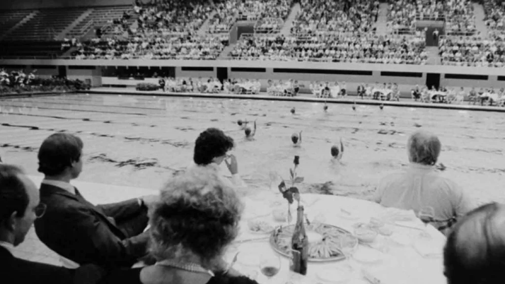 Spectators around a table watch as student swim in the 1983  Classic Splash in the Natatorium.