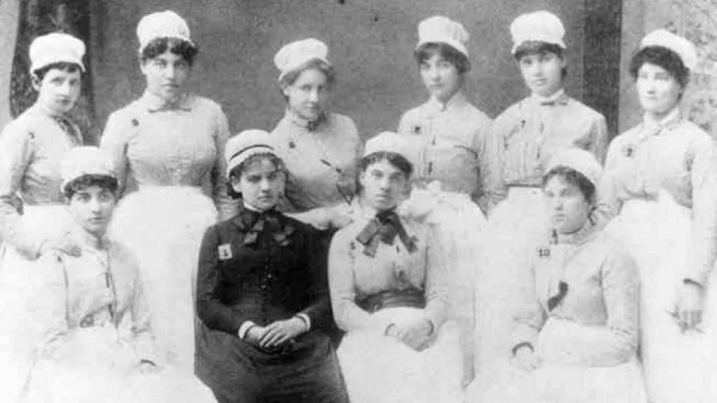 Members of the first graduating class of nursing, wearing uniforms, at Wishard Memorial Hospital in 1885 are posed in two rows.