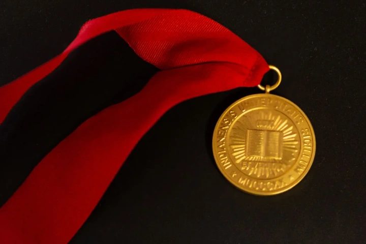 A gold IU medal strung on a red ribbon sits on a black velvet background.