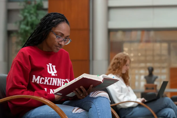 A female student wearing an IU sweatshirt studies a thick book in the McKinney School of Law atrium.