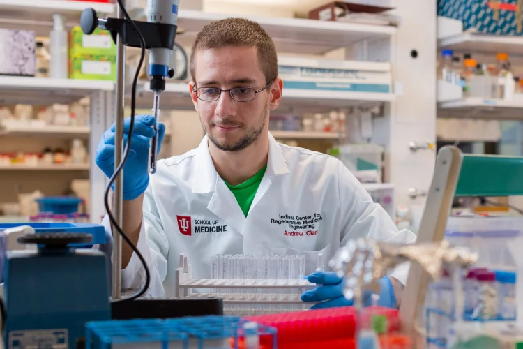 A male IU Medicine student researcher wearing protective equipment prepares samples in a colorful lab.