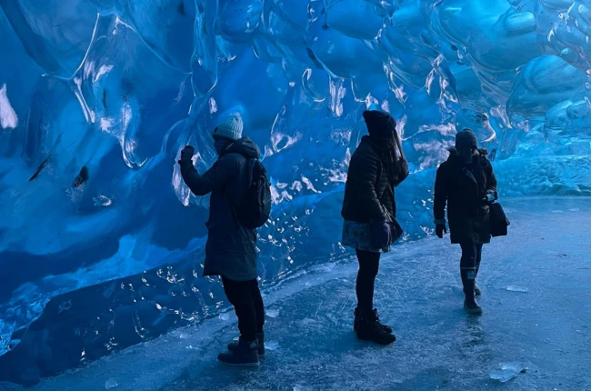 Three young women wearing heavy winter gear examine the inside of a glacier.