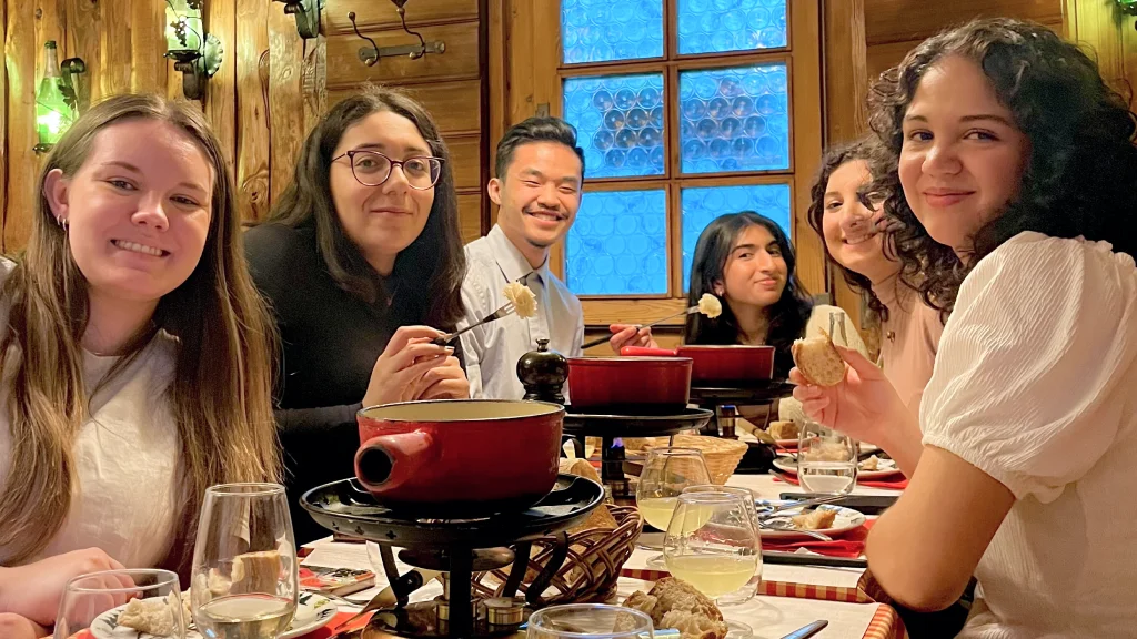 IU Indianapolis study abroad students gather around a table in a wooded Swiss restaurant dipping bread into cheese fondue pots.