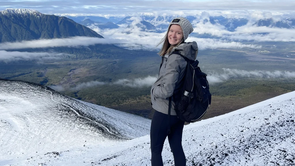 An IU Indianapolis student stands in hiking boots, winter outdoor gear, and a backpack on a mountain slope in Patagonia.