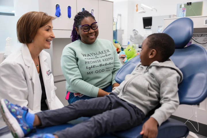 A woman and dentist look at a young boy sitting in a dentist chair for an appointment.