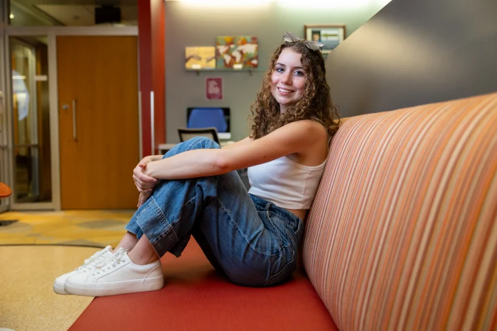 A student sits with legs up on a red striped upholstered banquette inside the IUI Honors College office.