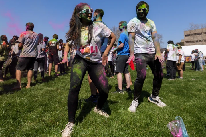 Two students covered in colorful chalk powder make some dance moves, while more students gather in the background for a Weeks of Welcome color event.