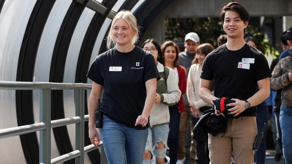 Two student tour guides with name tags on lead a group of family members and students through one of the enclosed pedestrian skywalks on the IUI campus.