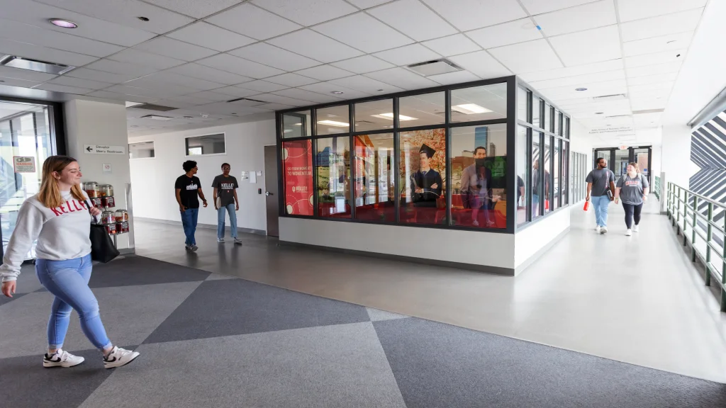 Students walking through a bright hallway with large windows and colorful wall art.