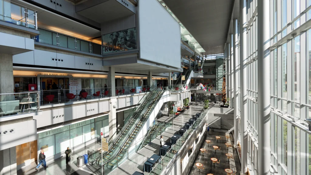 Bright, spacious atrium with multiple levels, escalators, glass railings, and floor-to-ceiling windows.