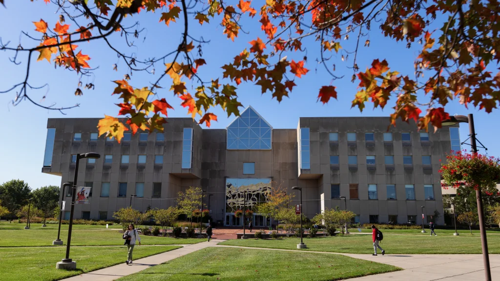 Modern university building framed by vibrant autumn leaves.