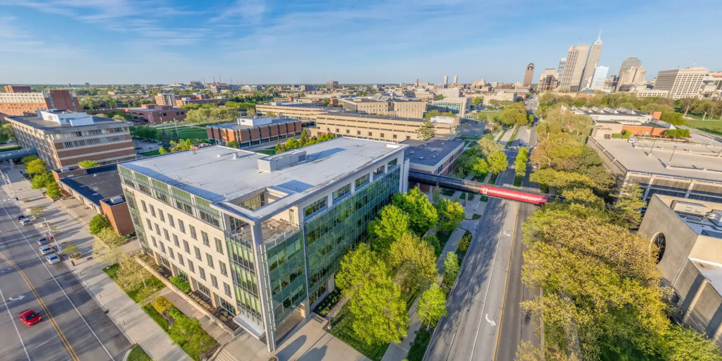 University Hall is seen from an elevated drone view, surrounded by lush green trees, with New York street leading through campus toward downtown Indianapolis, seen in the top right of the image.