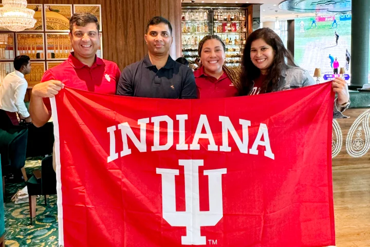 Four students or faculty hold up a red IU flag from one of the global gateway sites.