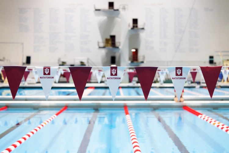 Red and white flags hang over lap lanes of the Natatorium; diving platforms are seen against the back wall in the distance.