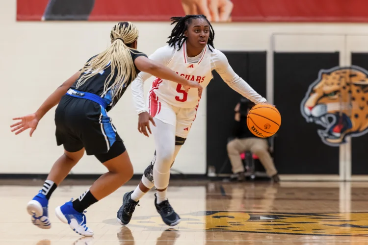 A member of the Jaguar women’s basketball team dribbles the ball down the court against an opponent.
