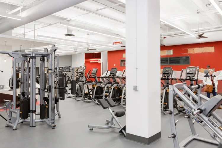 Cardio and weight machines stand against white columns and a red wall inside a fitness facility inside the Campus Center.