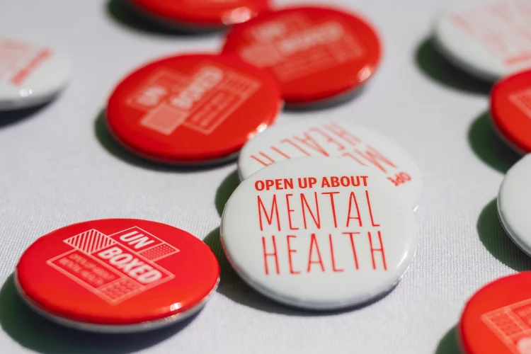 White and red buttons lie on a white surface; one says Open Up About Mental Health and the other says UnBoxed.