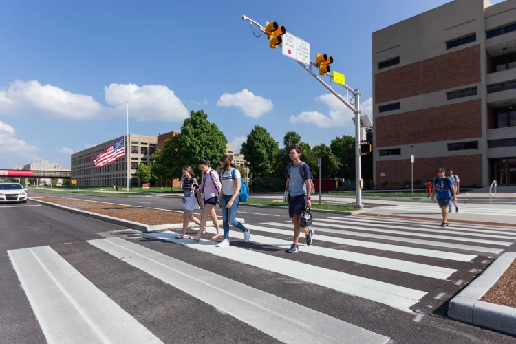 Students walk on a wide crosswalk with pedestrian-requested stop light s extended over the street to stop passing cars.