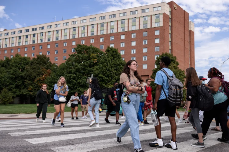 Students move in both directions of a crosswalk with University Tower seen in the background.