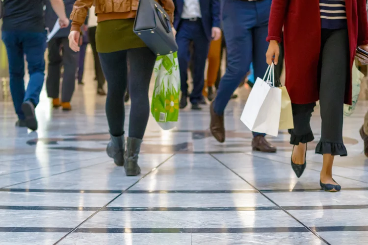Legs of people walking through a mall, some holding shopping bags.