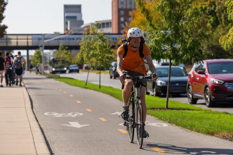 A helmeted cyclist bikes on a two-way paved bike lane on the IU Indianapolis campus.