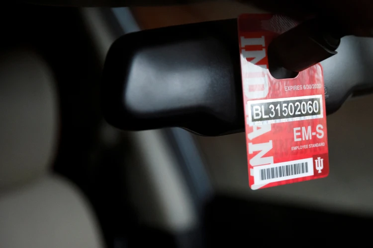 A red IU parking tag hangs with barcode and numbers hangs from the rear view mirror of a car.