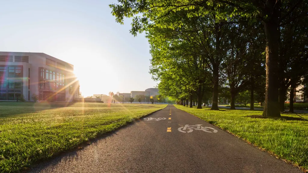 A bike path with a dotted yellow line extends into the distance; the sun rises beyond the science building to the left.