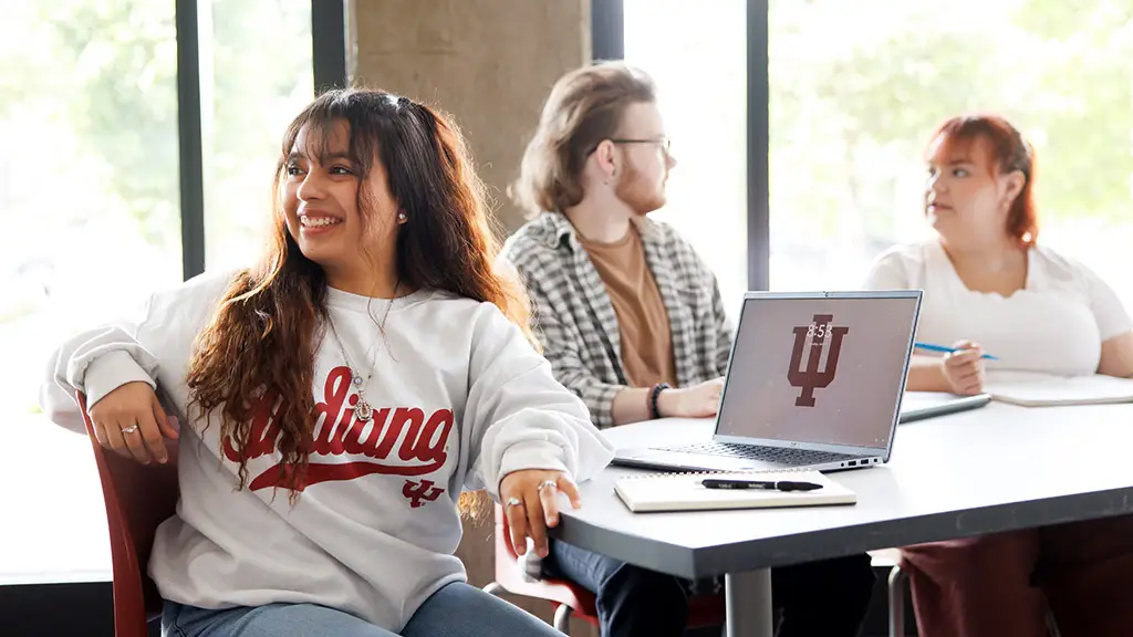 An IU Indianapolis student smiles toward the front of the classroom while two classmates sit behind her talking.