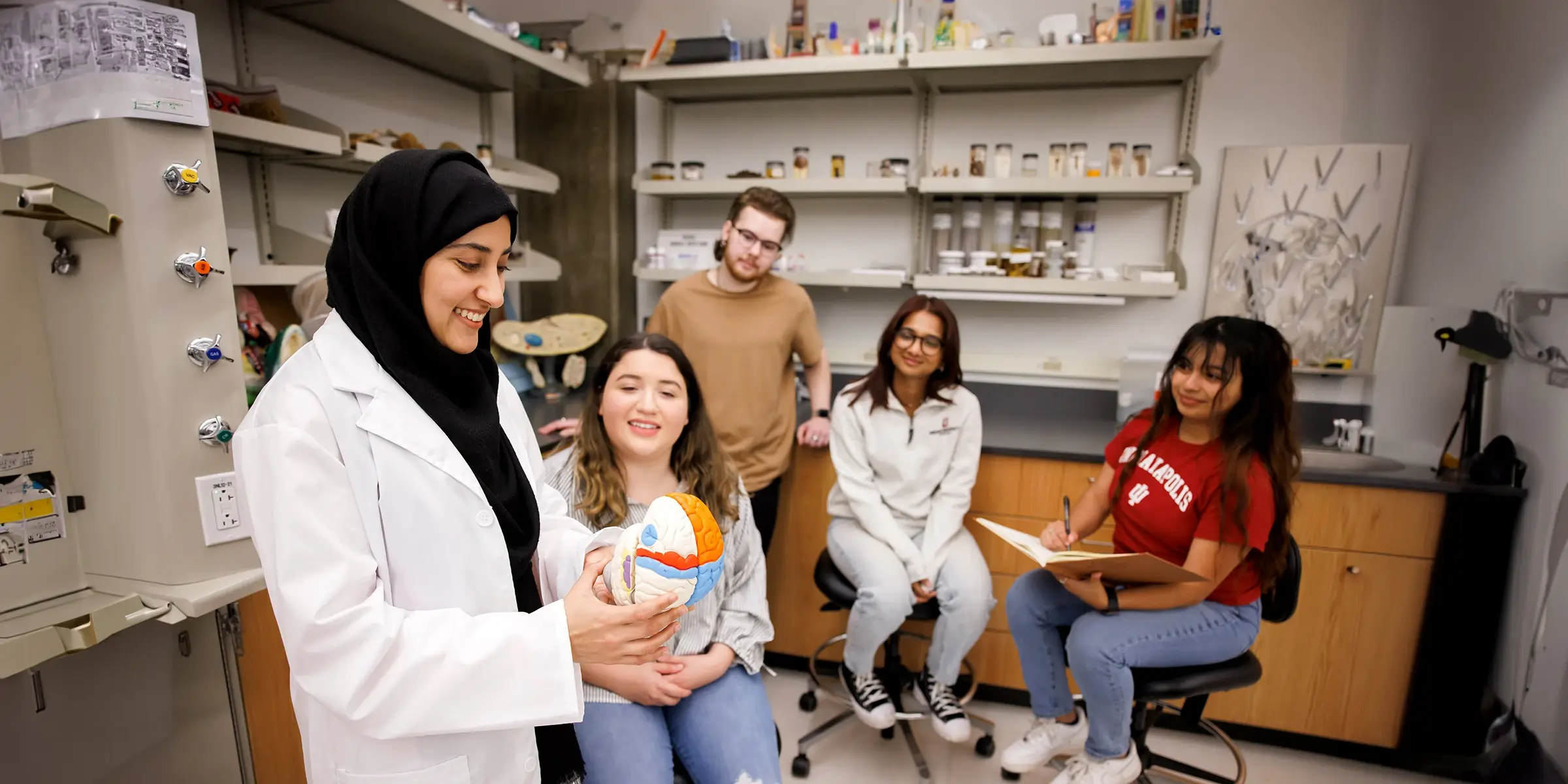 A female professor holds an anatomy model in front of a group of students.