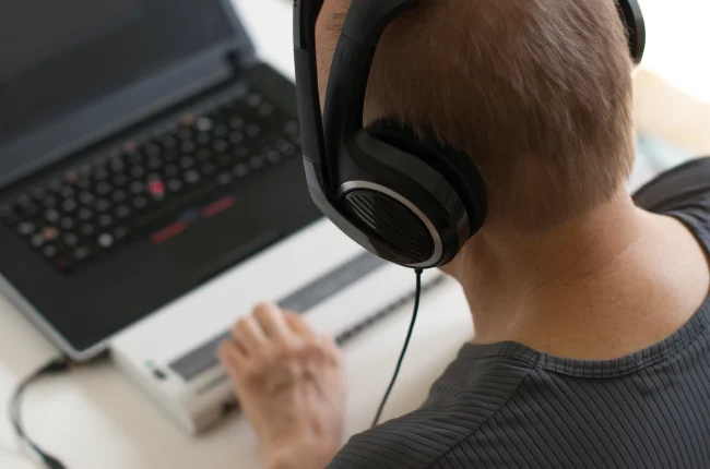 A person wearing headphones looks at a computer connected to an assistive technology screen reader.
