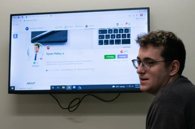 A sample ePortfolio website is shown on a tv monitor displayed on a wall with a man seated in front.