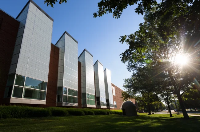 Sun shines through tree leaves outside Herron School of Art and Design.