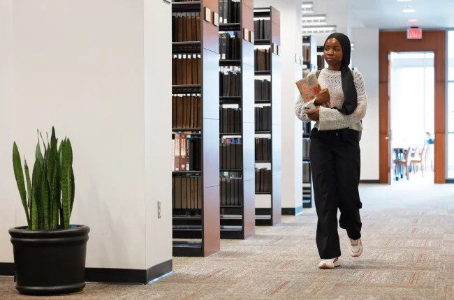 A student holding a book walks past bookshelves inside the Ruth Lilly Law Library