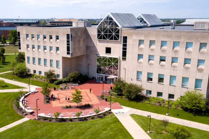 University Library is seen from an elevated position on a summer day, with student walking through the front bricked courtyard that holds outdoor seating.