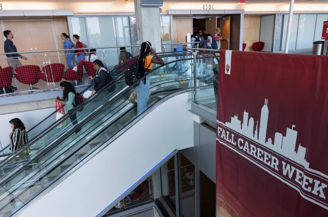Students move between floors of the Campus Center on escalators; a red banner hanging nearby says Fall Career Week.