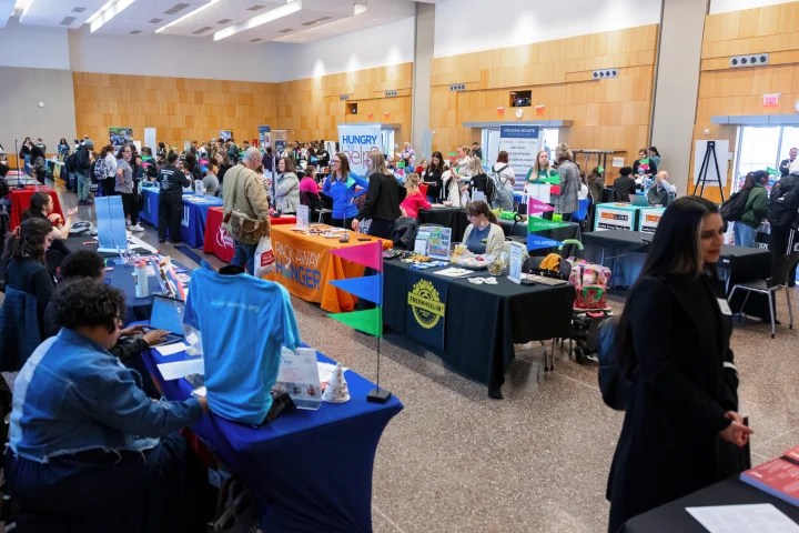 Student circulate in a large event space filled with tables displayed for handing out information about various businesses and organizations.