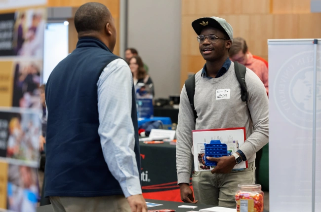 A young Black student in sporty casual wear chats with a recruiter at an IU Indianapolis career fair.